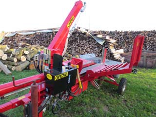 Roter Holzspalter-Anhänger im Garten vor einem Holzstapel 